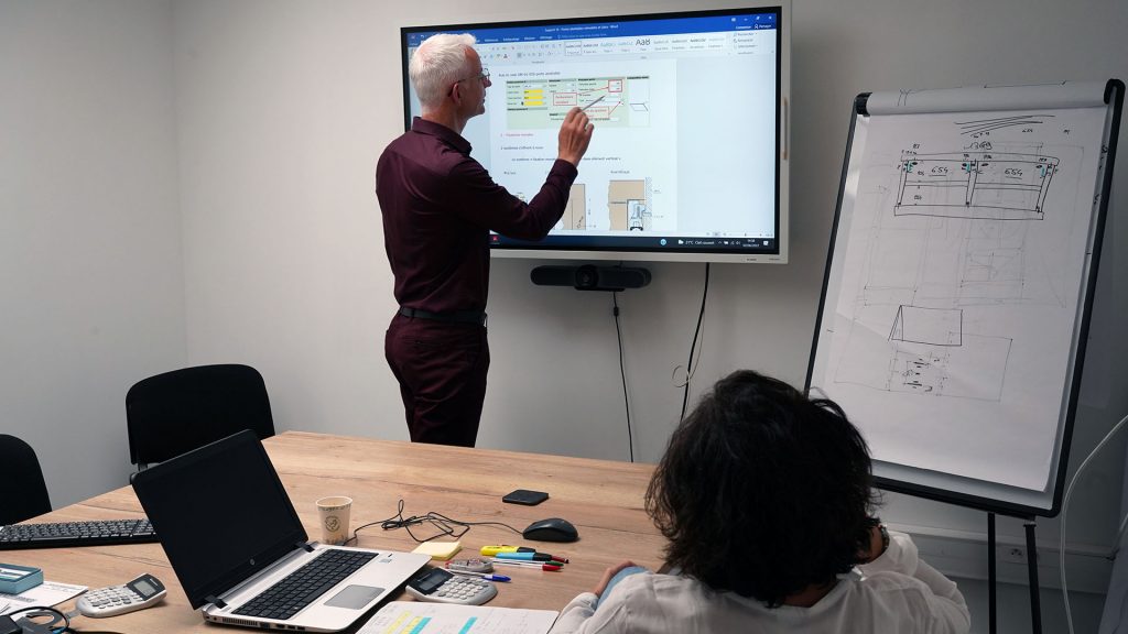 Dans une salle de réunion, le responsable formation annote un tableau sur un écran devant une nouvelle salariés